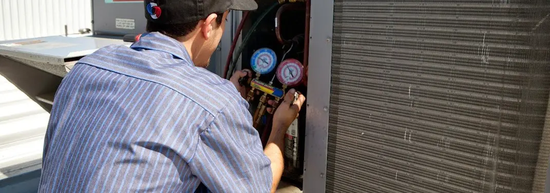 HVAC technician servicing a condenser unit in Brock Hall